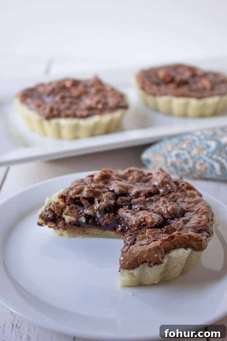 Decadent Chocolate Walnut Tart Recipe 5 A mini chocolate tart with a slice missing.
