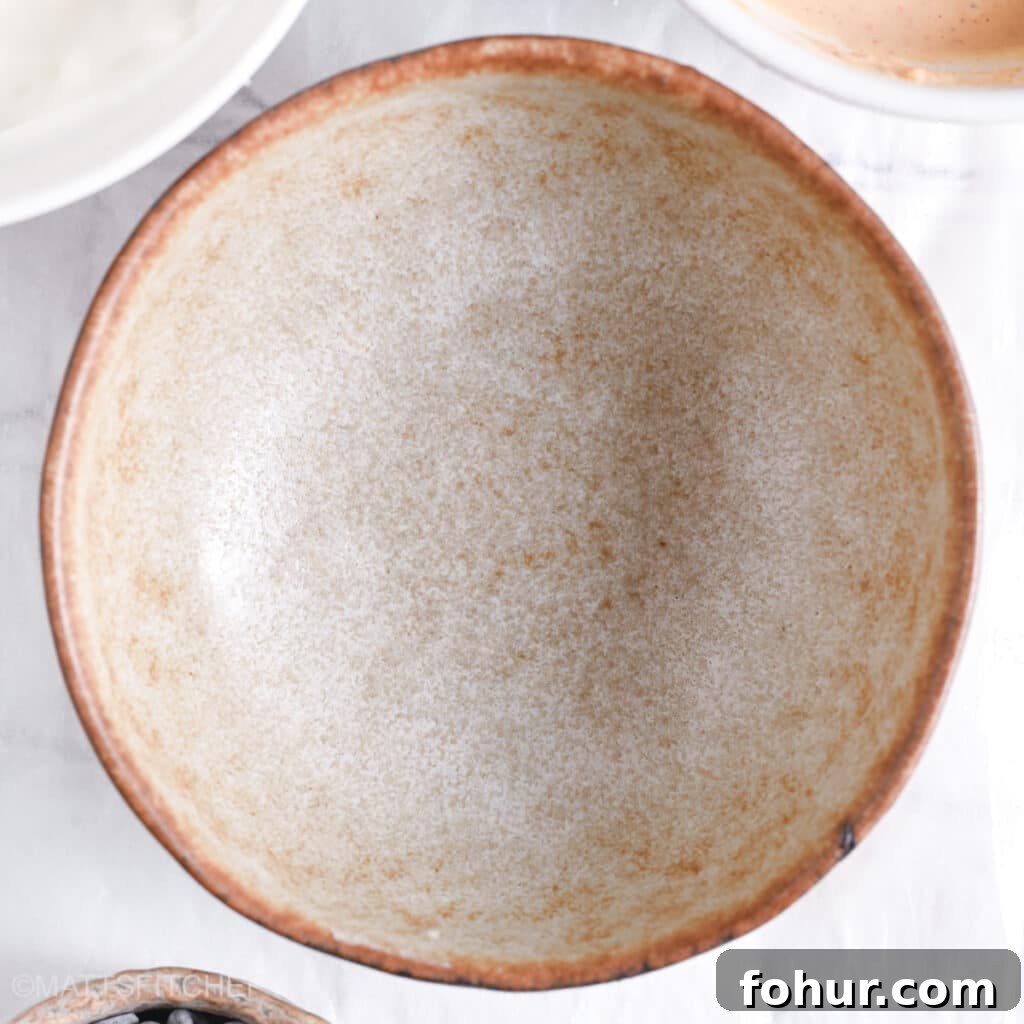 No-Bake Edible Protein Cookie Dough Recipe 3 A clean, empty ceramic mixing bowl placed on a white surface, ready for ingredients.