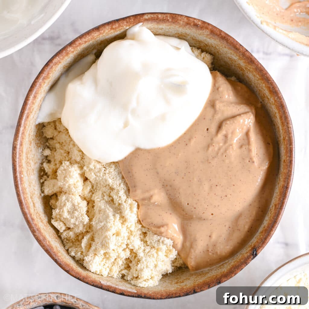No-Bake Edible Protein Cookie Dough Recipe 6 A dollop of thick Greek yogurt sitting on top of protein powder and peanut butter in a bowl.