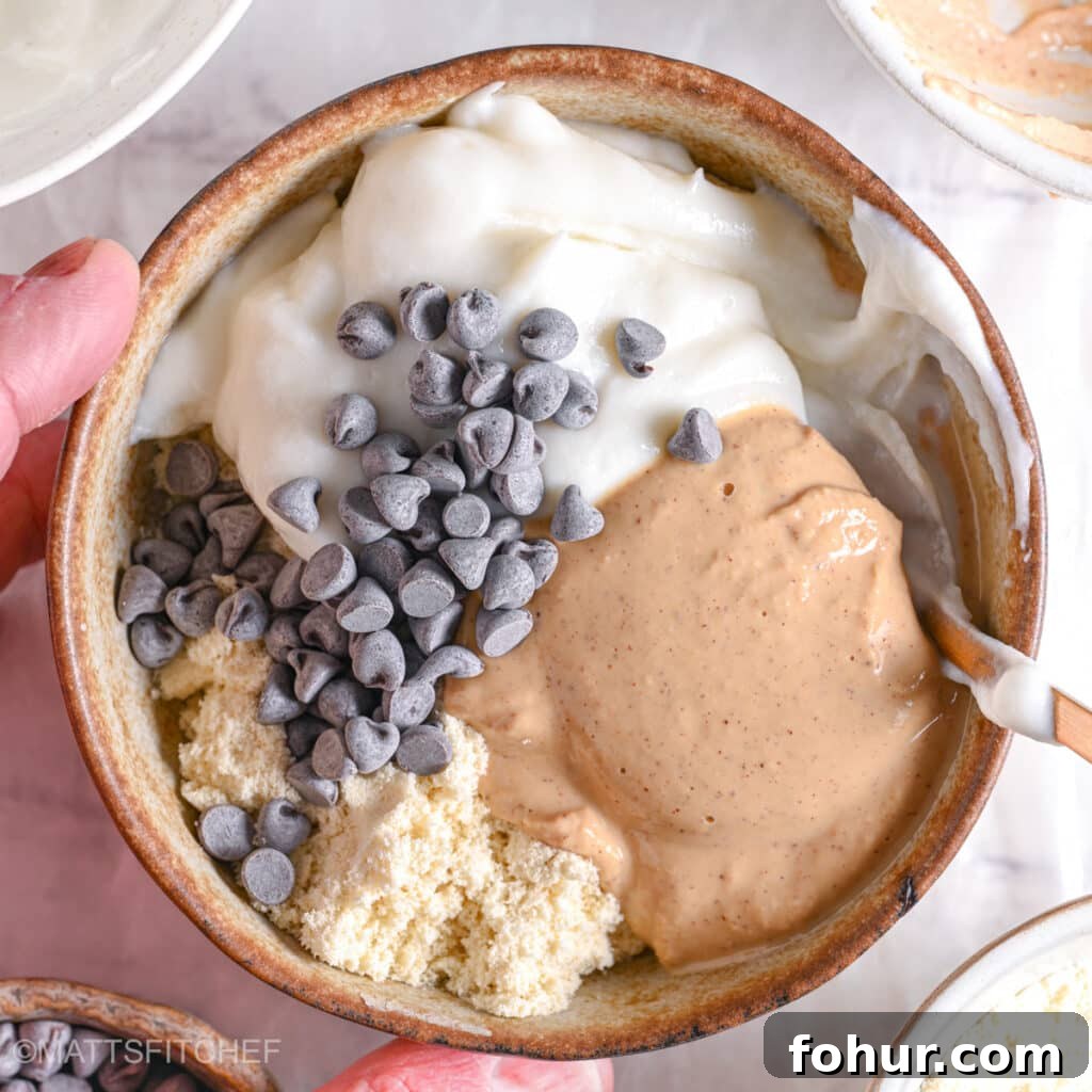 No-Bake Edible Protein Cookie Dough Recipe 8 A golden spoon beginning to mix protein powder, peanut butter, Greek yogurt, and chocolate chips.