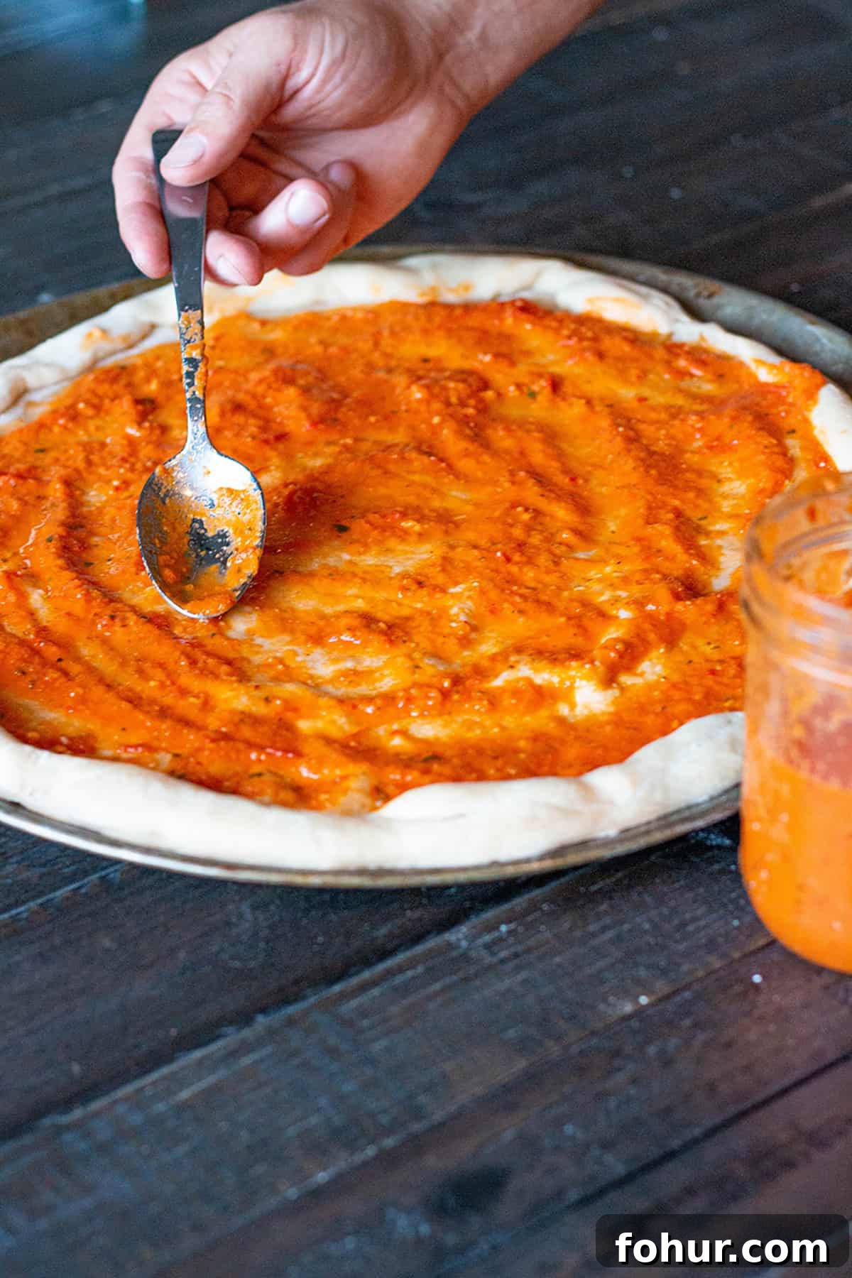 Fresh homemade pizza dough with homemade pizza sauce being spread on it. 