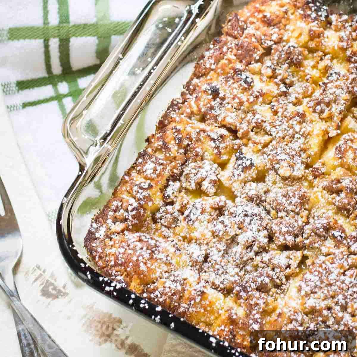 Brioche Baked French Toast with Butterscotch Sauce 9 Overhead shot of french toast bake sprinkled with powdered sugar in a clear baking dish.