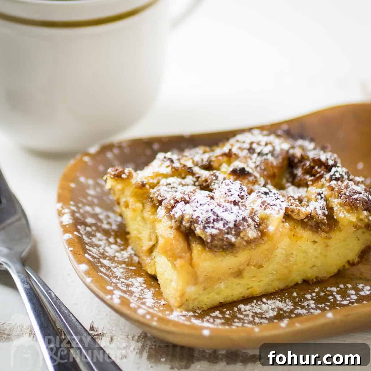 Brioche Baked French Toast with Butterscotch Sauce 8 Side shot of brioche french toast on a brown plate sprinkled with powdered sugar with a fork on the side.