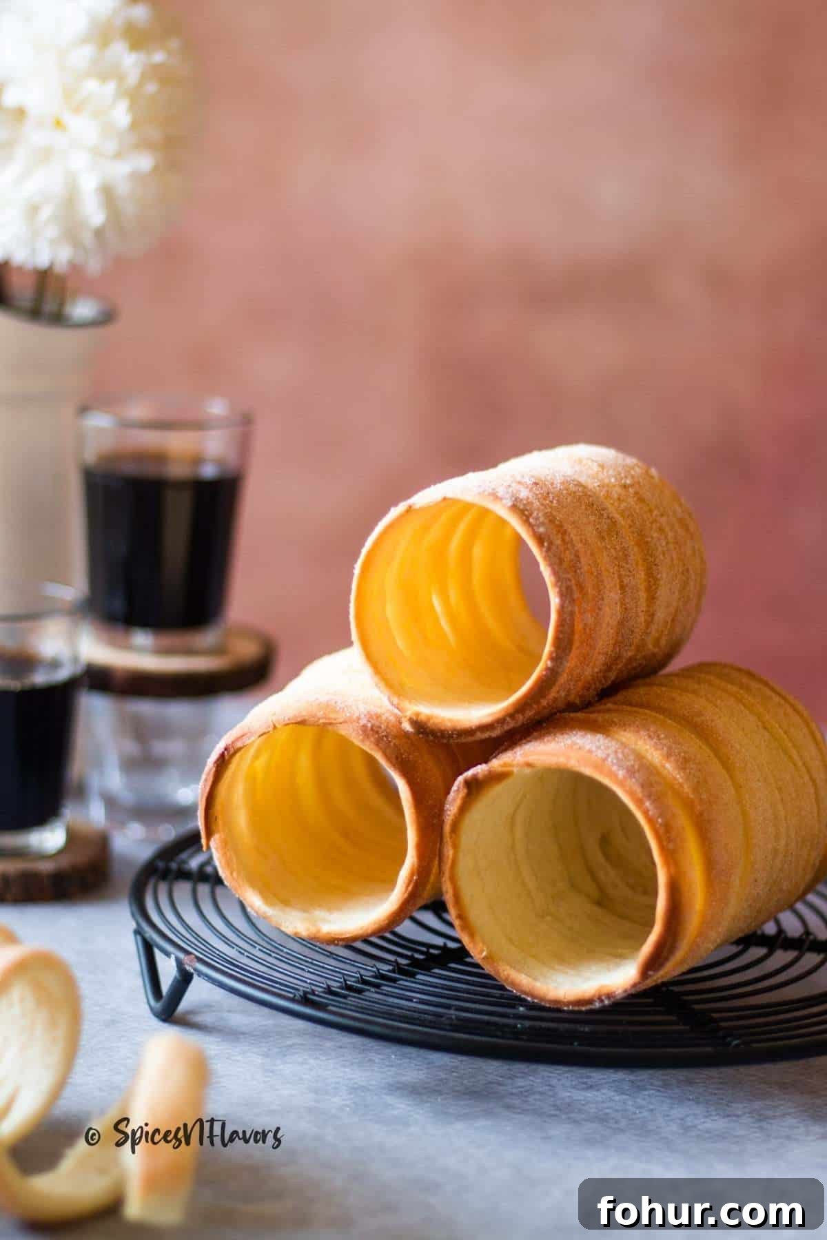 How to Make Authentic Hungarian Chimney Cake (Kürtőskalács) 2 three chimney cakes stacked like a pyramid on a wire stand with coffee in the background