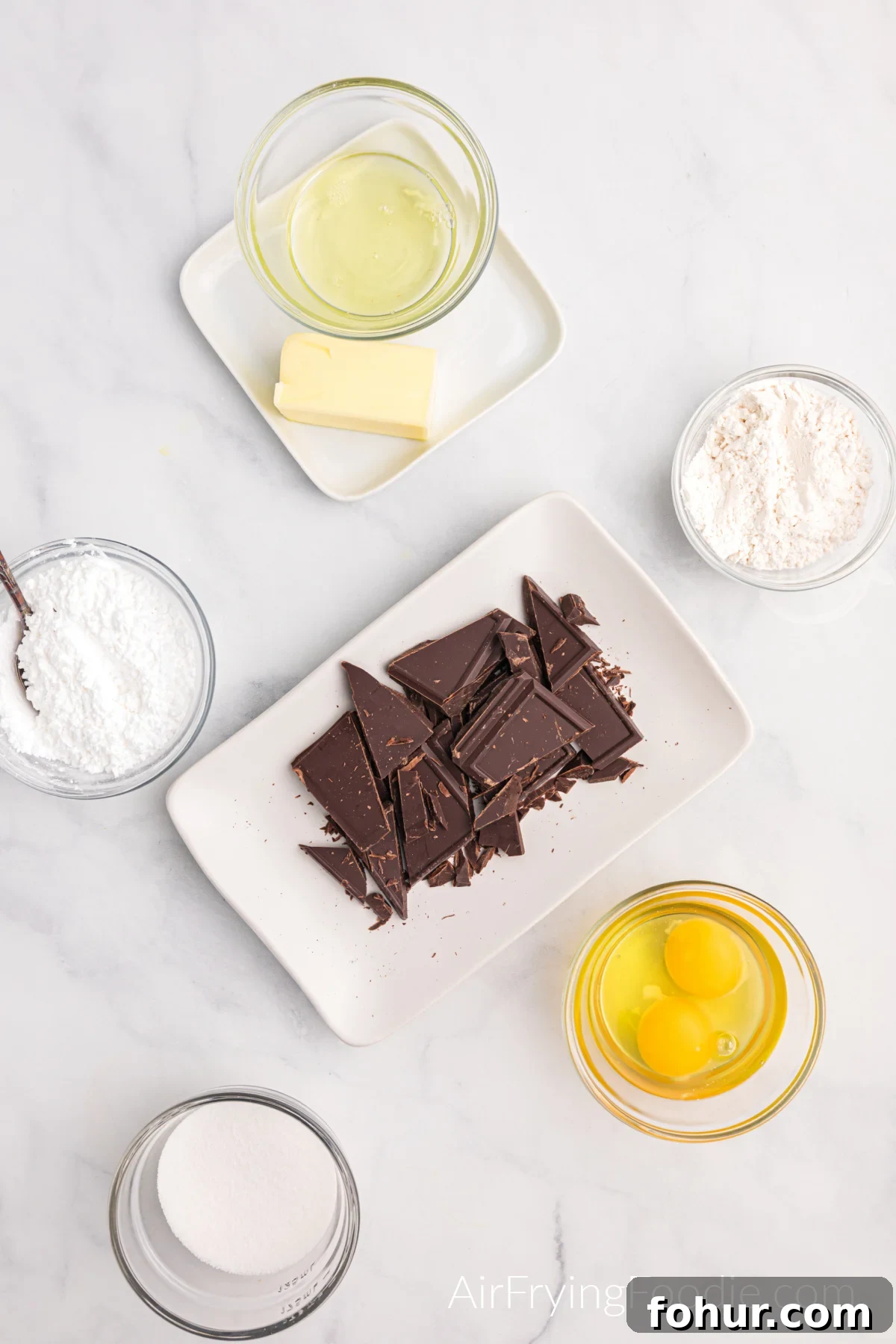 Ingredients needed to make air fryer lava cake measured in glass bowls on a marble table. 
