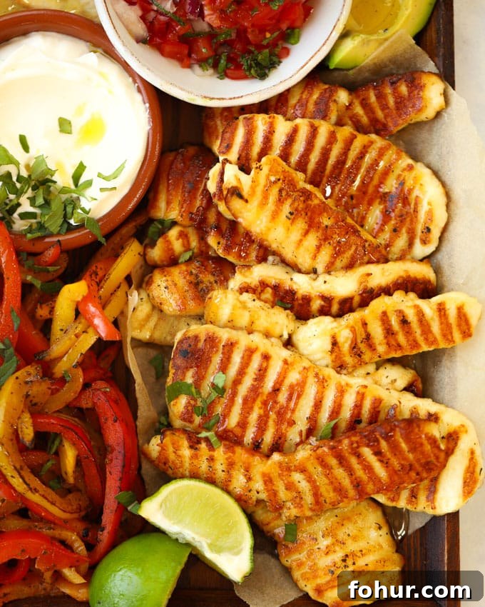 15-Minute Halloumi Fajitas with Peppers and Onions 3 Grilled halloumi with griddle lines on, on a tray with vegetables, lime, sour cream and wraps for the recipe Halloumi Fajitas.
