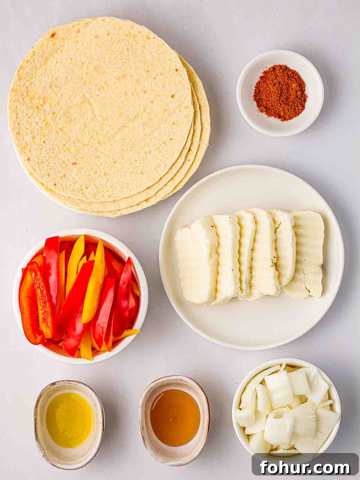 15-Minute Halloumi Fajitas with Peppers and Onions 4 The ingredients for halloumi fajitas laid out in plates and bowls on a white counter top.