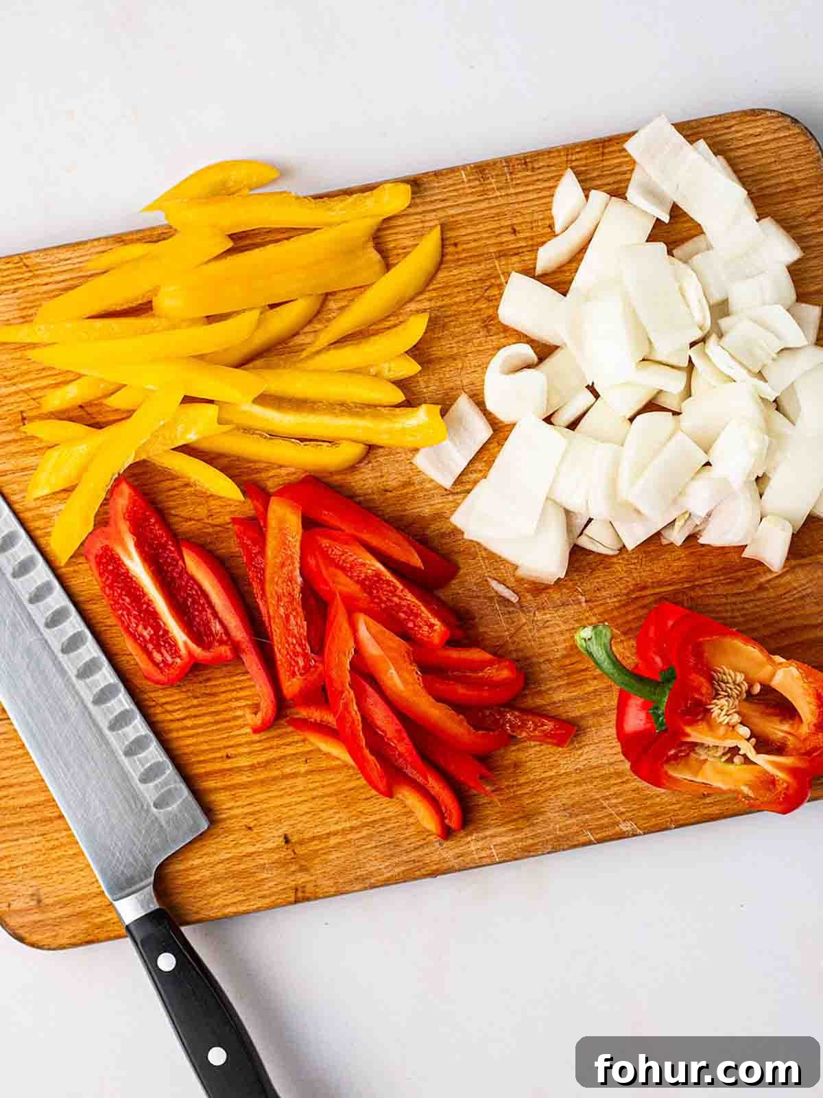 15-Minute Halloumi Fajitas with Peppers and Onions 5 Peppers and onions sliced on a chopping board with a knife to the side for step 1 in the recipe for Halloumi Fajitas.