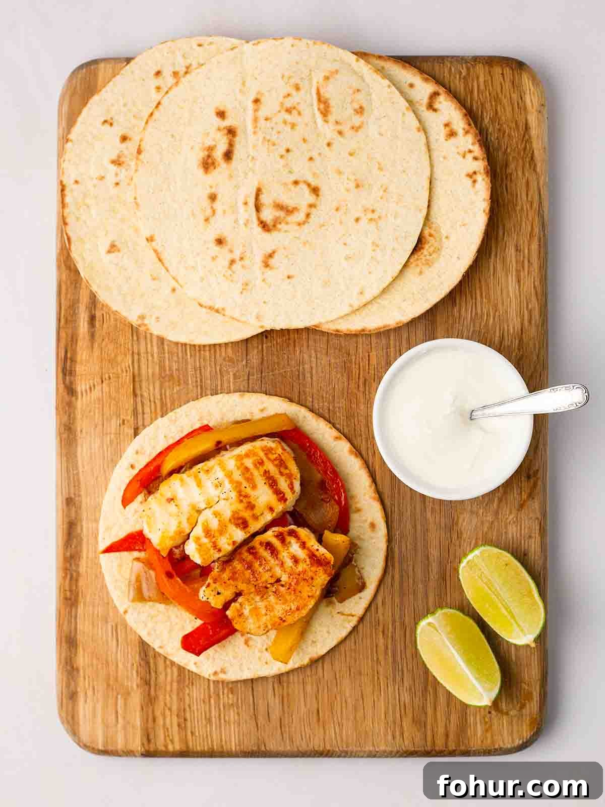 15-Minute Halloumi Fajitas with Peppers and Onions 8 Wraps on a chopping with, one filled with halloumi fajitas and yoghurt dip to the side.