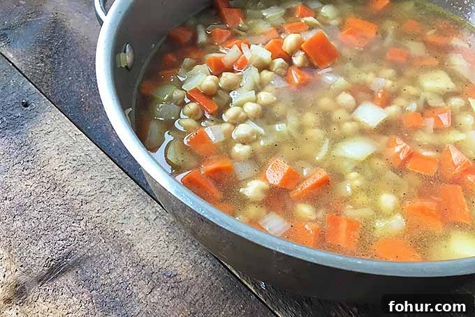 Creamy Saffron Chickpea Stew Recipe 7 A pot of broth with beans, carrots, and onions
