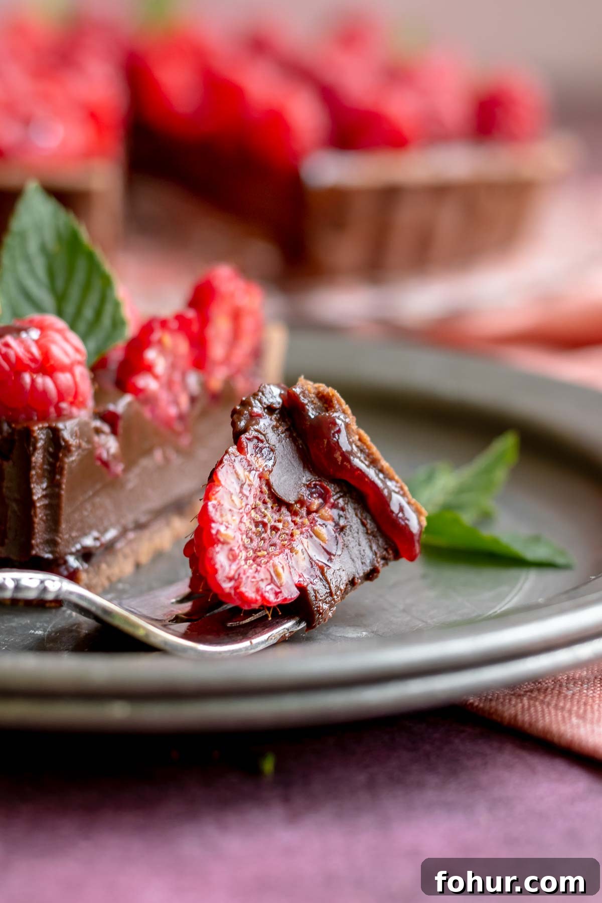From Scratch Chocolate Raspberry Tart Recipe 11 A piece of chocolate tart sits on a fork with a raspberry piece in it.