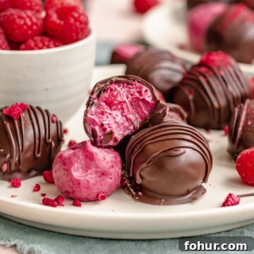 Raspberry truffles stacked on plate. One has a bite removed.