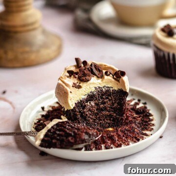 Mocha cupcake on a plate with a bite removed sitting on a spoon.