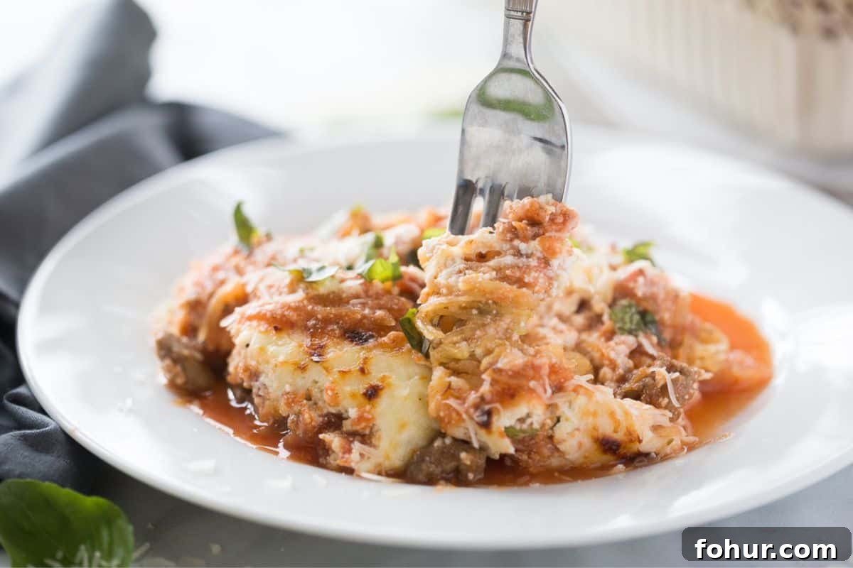 Low-Carb Spaghetti Squash Lasagna Recipe 2 A fork full of spaghetti squash lasagna on a white plate with sauce, ricotta cheese, and fresh basil.