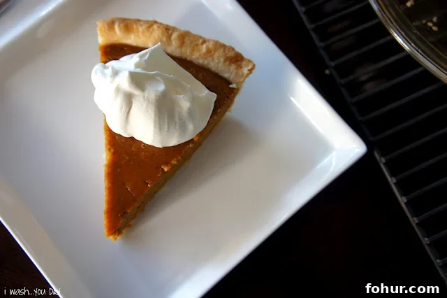 A slice of pumpkin pie on a square plate topped with a dollop of whipped cream