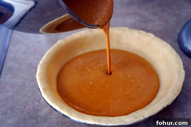Pumpkin pie batter being poured into a raw pie shell