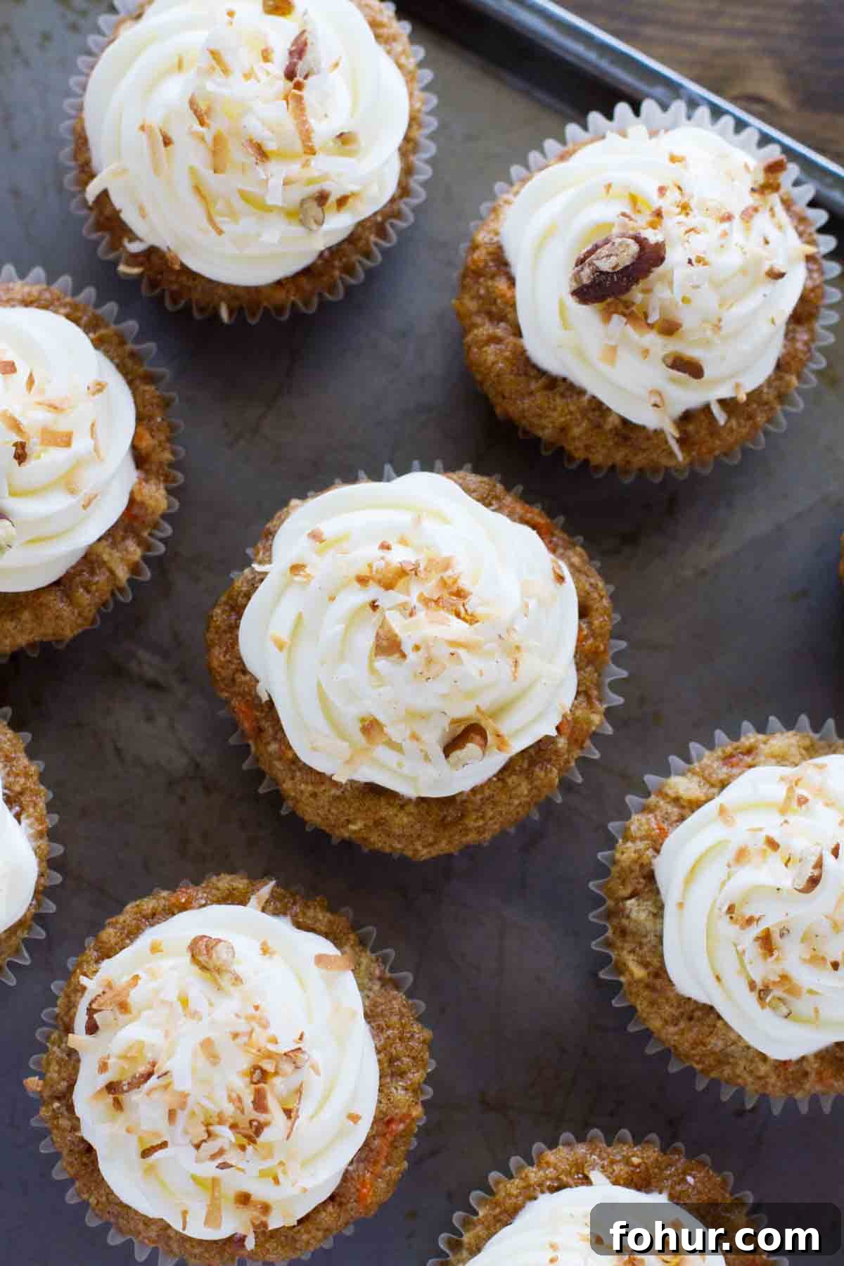 Simply the best, these Carrot Cake Cupcakes are filled with lots of carrots and coconut and are topped with a smooth and creamy cream cheese frosting. overhead view of carrot cake cupcakes on a baking sheet