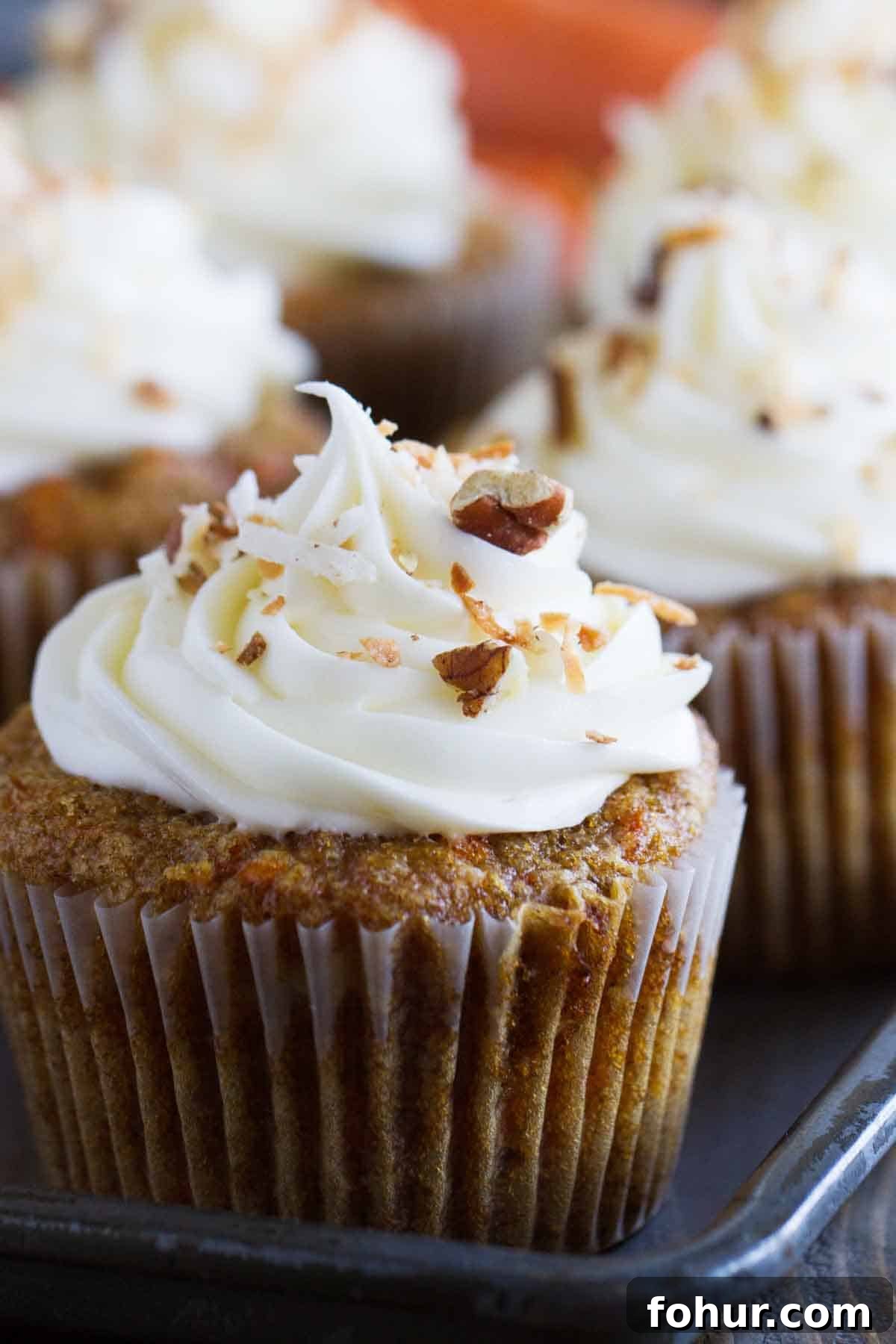 Simply the best, these Carrot Cake Cupcakes are filled with lots of carrots and coconut and are topped with a smooth and creamy cream cheese frosting. close up of carrot cake cupcake topped with cream cheese frosting, nuts, and coconut