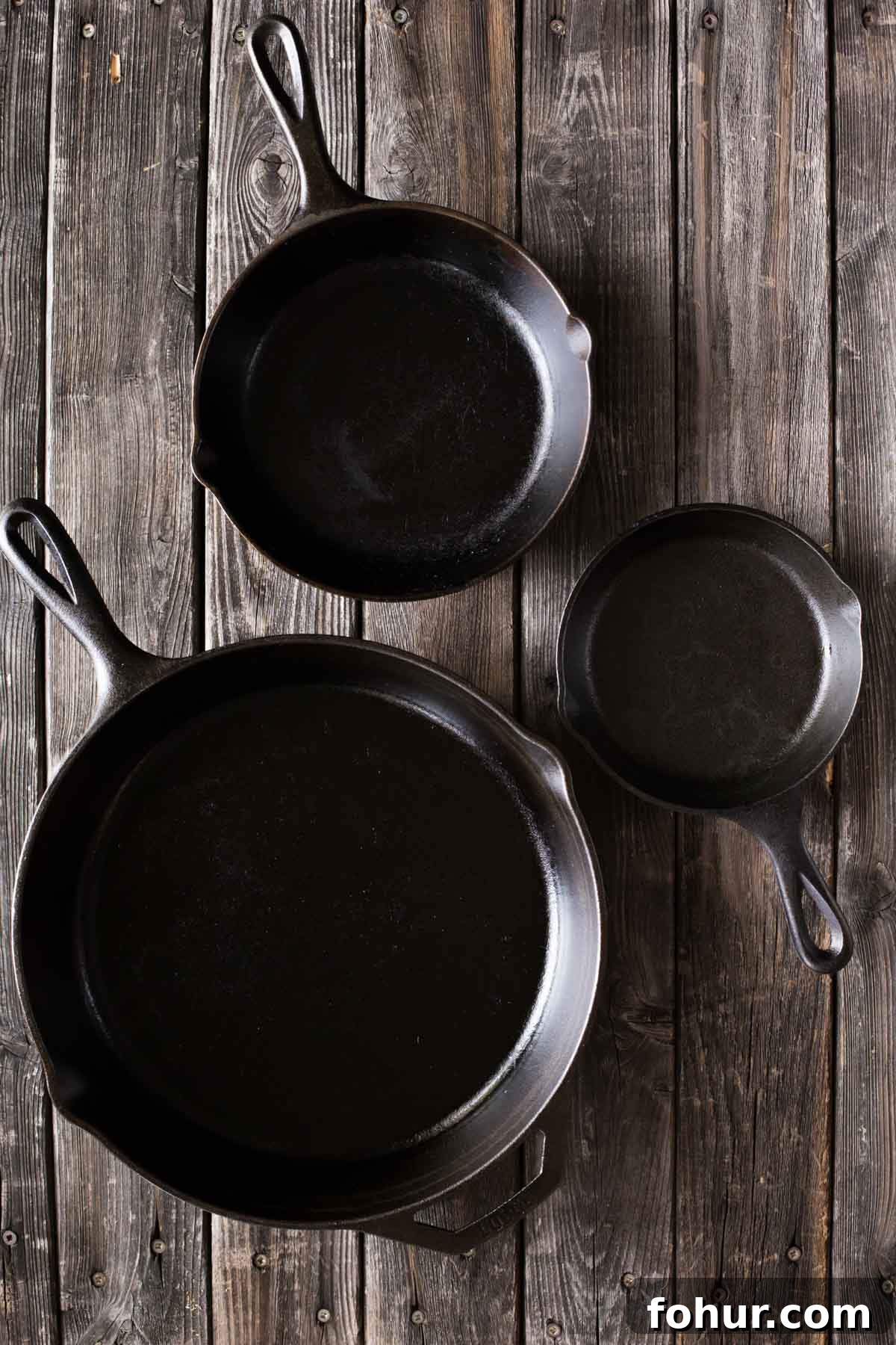 How to Clean a Cast Iron Skillet Without Stripping Seasoning 3 A top down view of a small, medium, and large sized cast iron skillet on a wooden background.