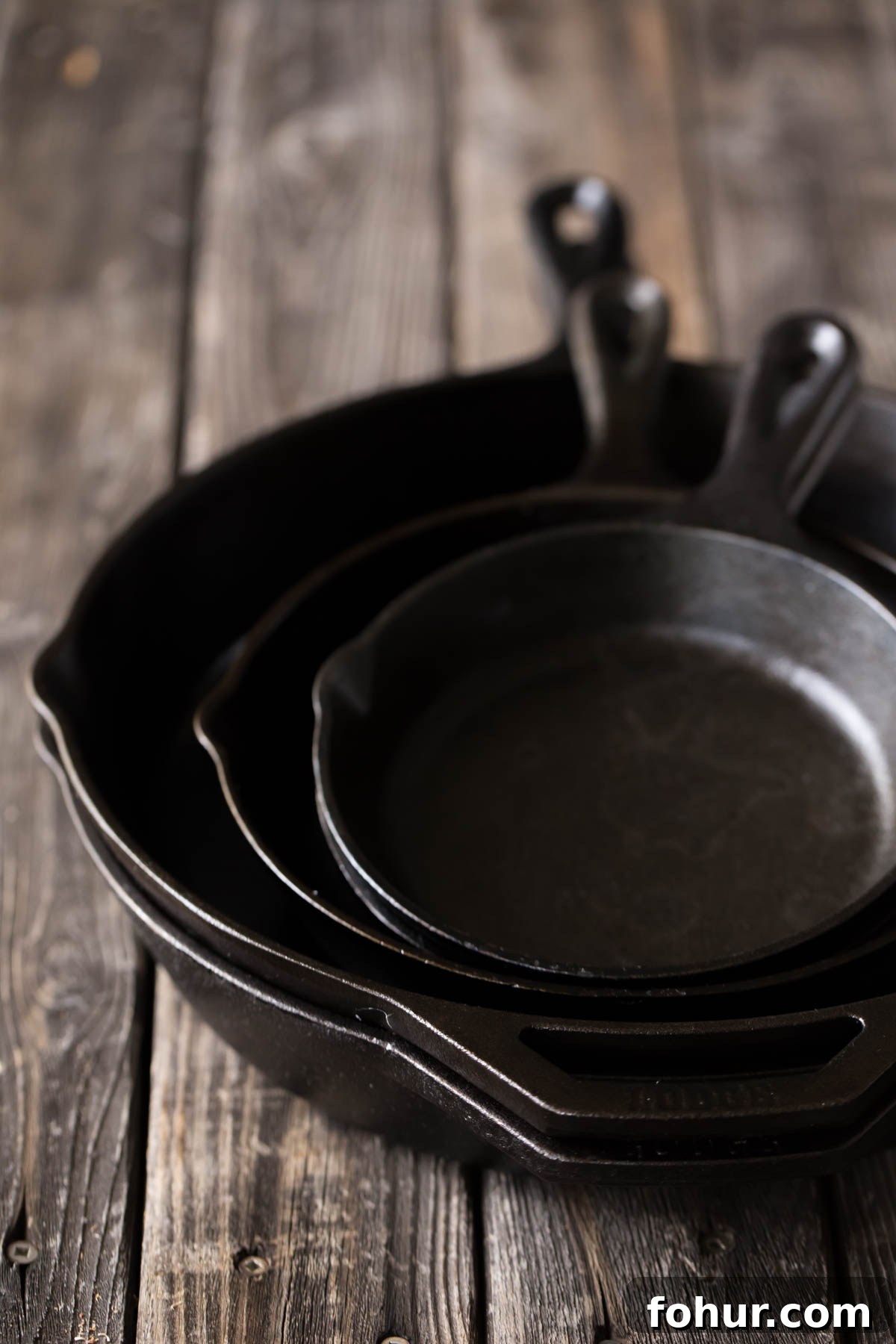 How to Clean a Cast Iron Skillet Without Stripping Seasoning 4 Five cast iron skillets stacked on a wooden board.
