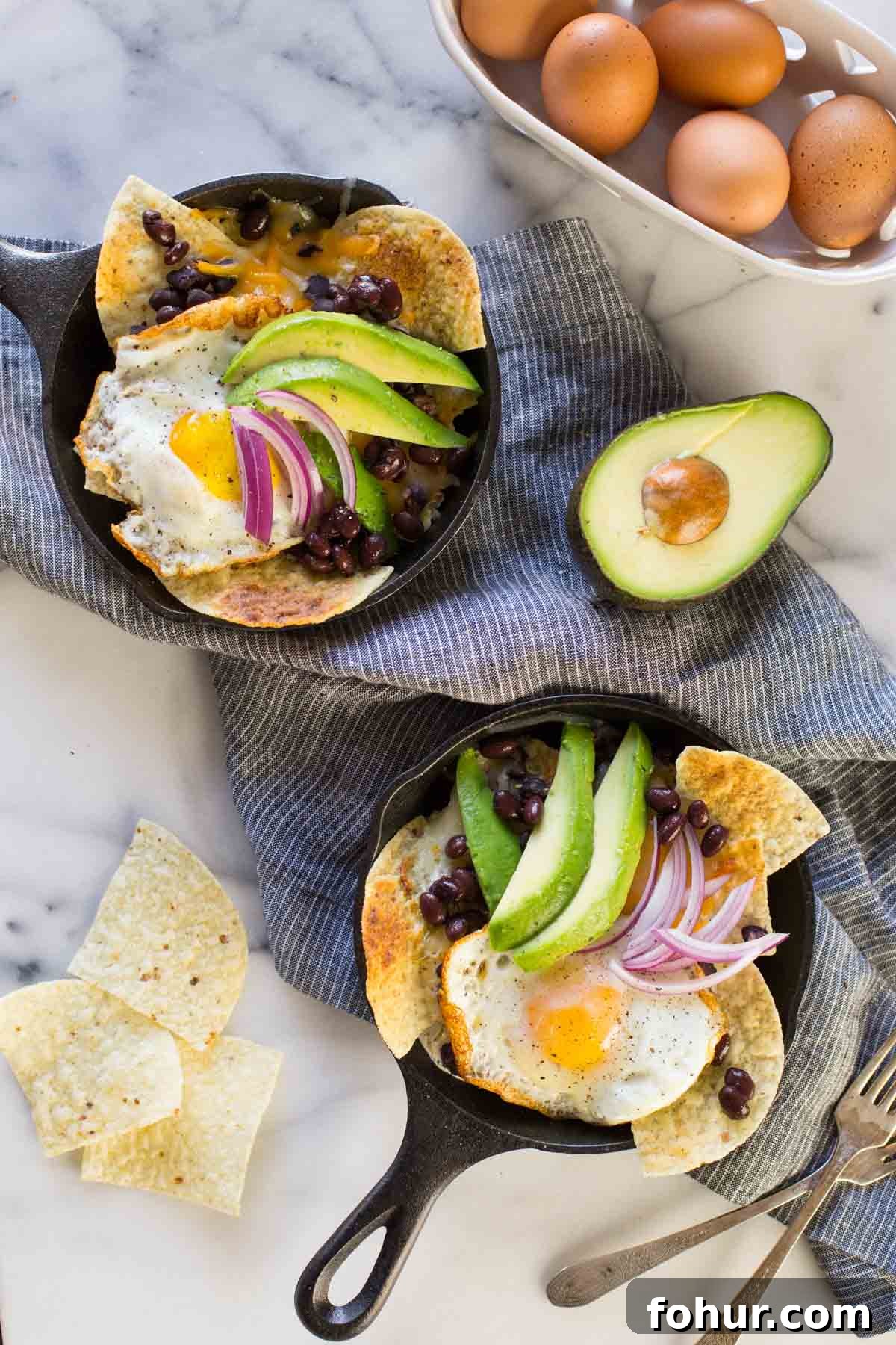 How to Clean a Cast Iron Skillet Without Stripping Seasoning 6 Two Breakfast Nacho Skillets topped with avocado slices and red onions, with a few tortilla chips, a half of an avocado, a basket of eggs and two forks sitting next to the skillets.