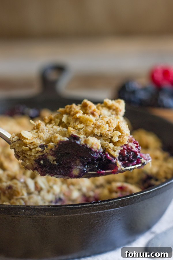How to Clean a Cast Iron Skillet Without Stripping Seasoning 9 Triple Berry Skillet Crisp on a serving spoon, with the cast iron skillet of Triple Berry Skillet Crisp in the background.