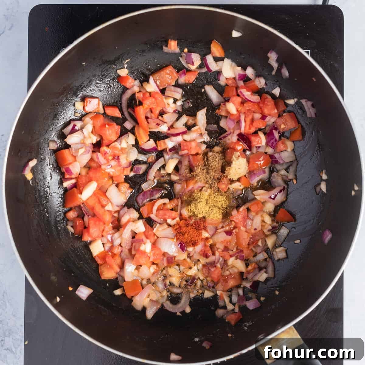 Gomen Wat: Spicy Ethiopian Collard Greens Recipe 6 Overhead view of a skillet pan with simmered onions, oil, tomatoes, ginger paste, cumin powder, and paprika.