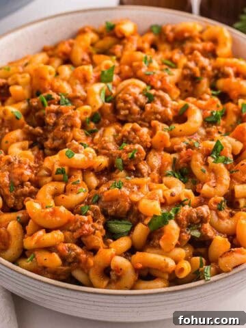 A bowl filled with American goulash with elbow macaroni ground beef and tomato sauce and topped with chopped parsley.