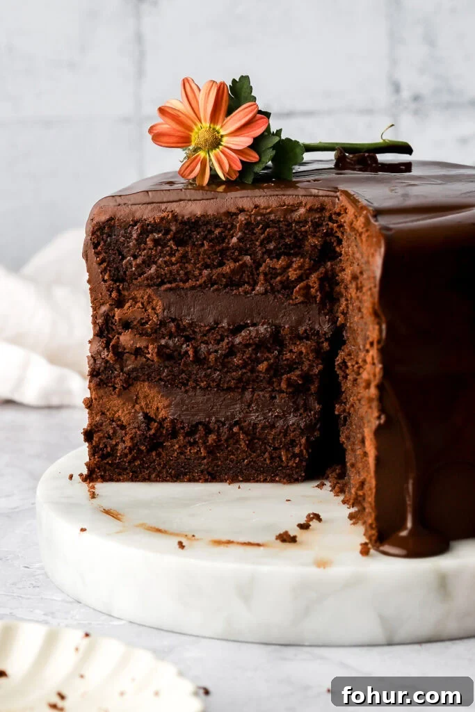 Decadent Chocolate Ganache Cake Recipe 2 dark chocolate cake layered frosted with chocolate ganache and chocolate drip, slice missing showing the inside