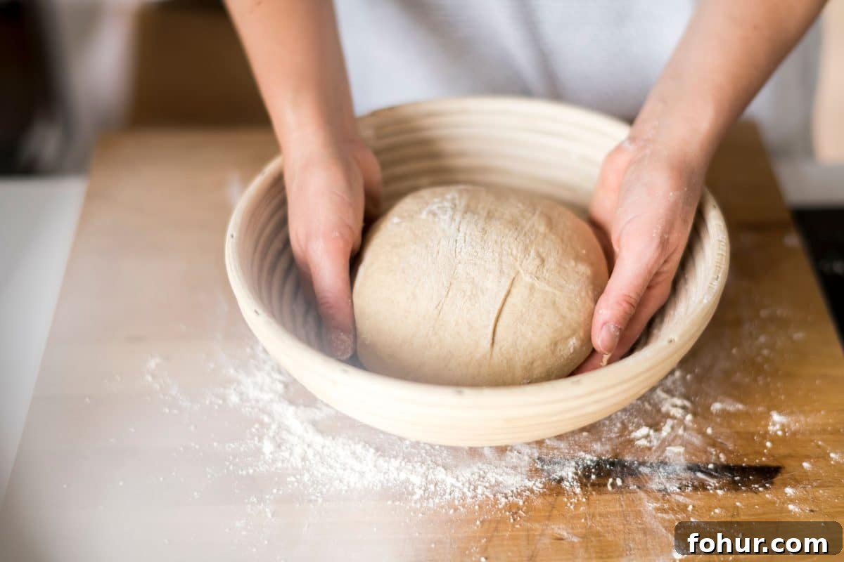 A ball of dough shaped and being placed in a banneton basket for fermentation. Hostess At Heart
