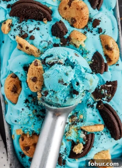 Ice cream scoop with a big scoop of blue cookie monster ice cream on top of loaf pan filled with ice cream.