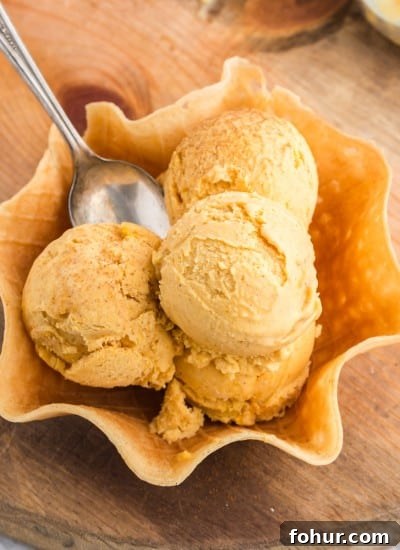three scoops of pumpkin ice cream piled in a waffle cone bowl with spoon.