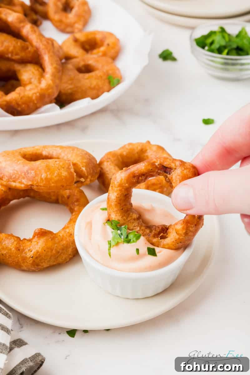 Crispy Gluten-Free Onion Rings Recipe 5 a small plate of onion rings and a cup of pinkish creamy dip. A hand is dipping one onion ring into the dip