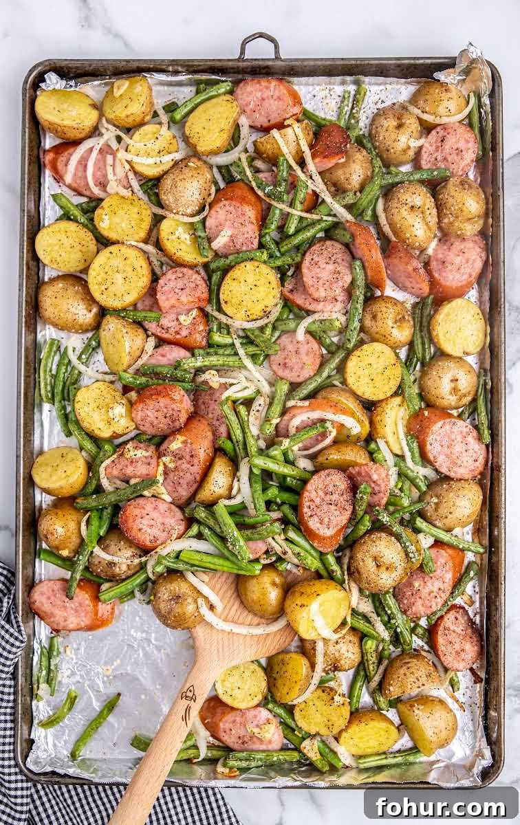 One-Pan Sausage, Green Bean and Potato Casserole 7 close up overhead shot of Sausage Green Bean Potato Casserole on a sheet pan with a wooden spoon
