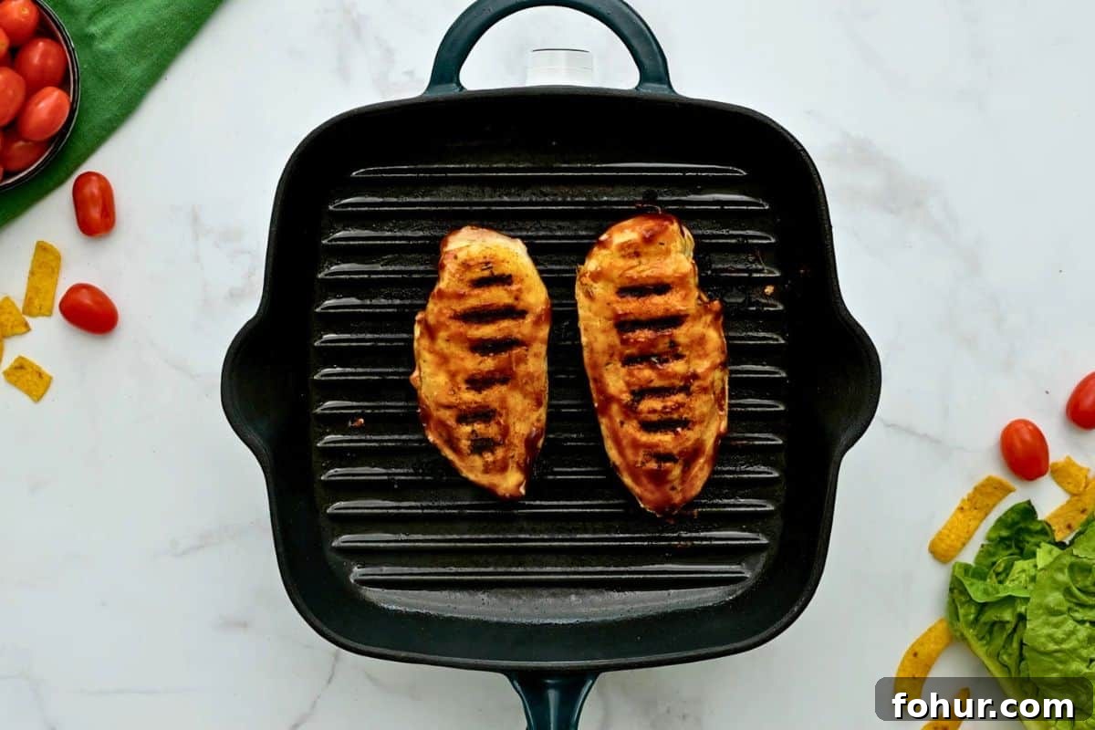 Two seasoned chicken breasts brushed with tomato based BBQ sauce on grill plate for BBQ Chicken Salad.