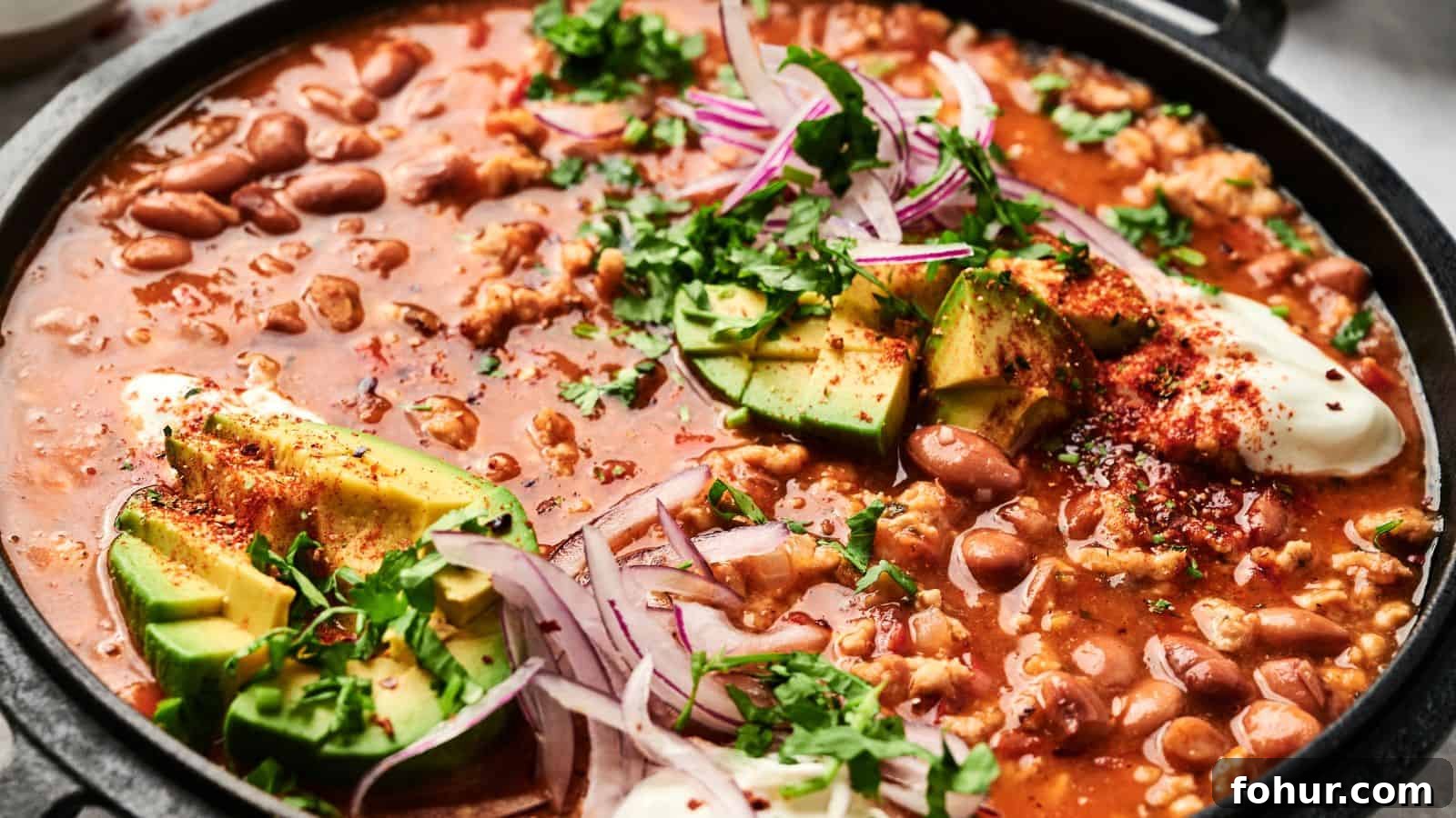 31 New Year's Eve Snacks for Late-Night Parties 11 A close-up of a pot of chili with beans, avocado slices, red onion, sour cream, and garnished with chopped cilantro.