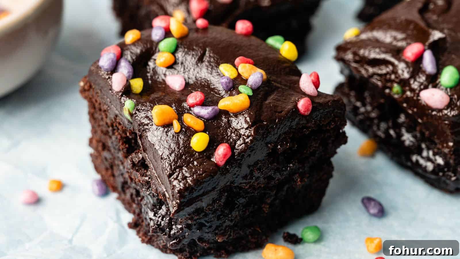 31 New Year's Eve Snacks for Late-Night Parties 14 Close-up of a thick, fudgy chocolate brownie topped with colorful candy sprinkles on a light blue surface.
