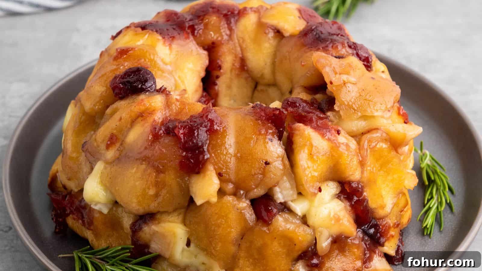 31 New Year's Eve Snacks for Late-Night Parties 15 A baked pull-apart bread ring with melted cheese and cranberries on a gray plate, garnished with rosemary sprigs.
