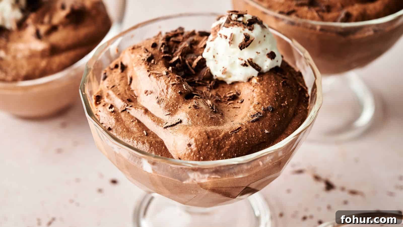 31 New Year's Eve Snacks for Late-Night Parties 29 A glass dessert cup filled with chocolate mousse, topped with whipped cream and chocolate shavings, placed on a light-colored surface.