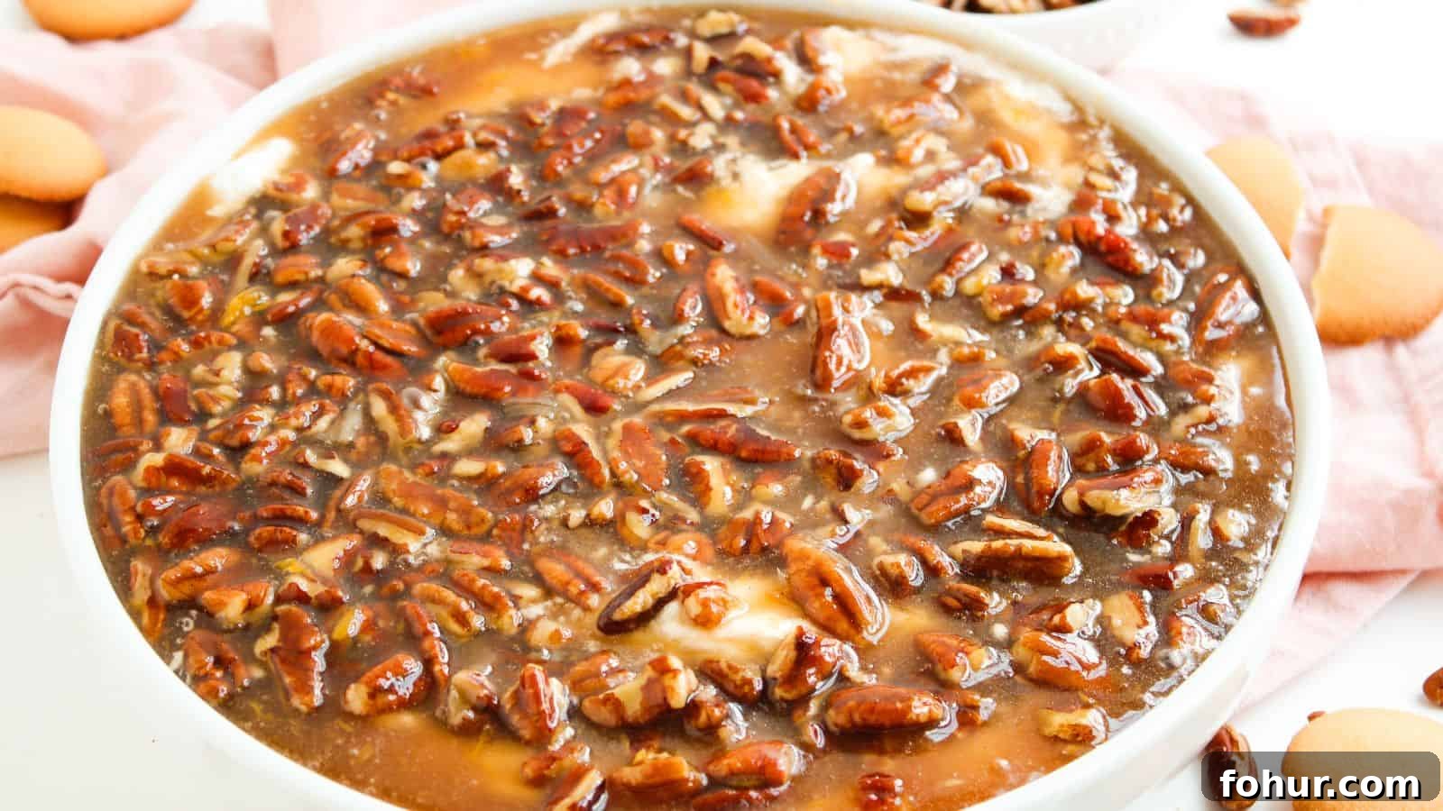 31 New Year's Eve Snacks for Late-Night Parties 8 A close-up of a dessert topped with a glossy layer of pecans and caramel sauce in a white dish, with vanilla wafers on the side.