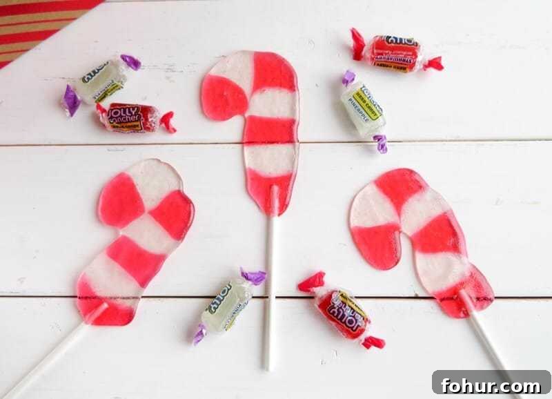 Candy cane shaped suckers on white wood background with strawberry and pineapple jolly rancher candies scattered around.