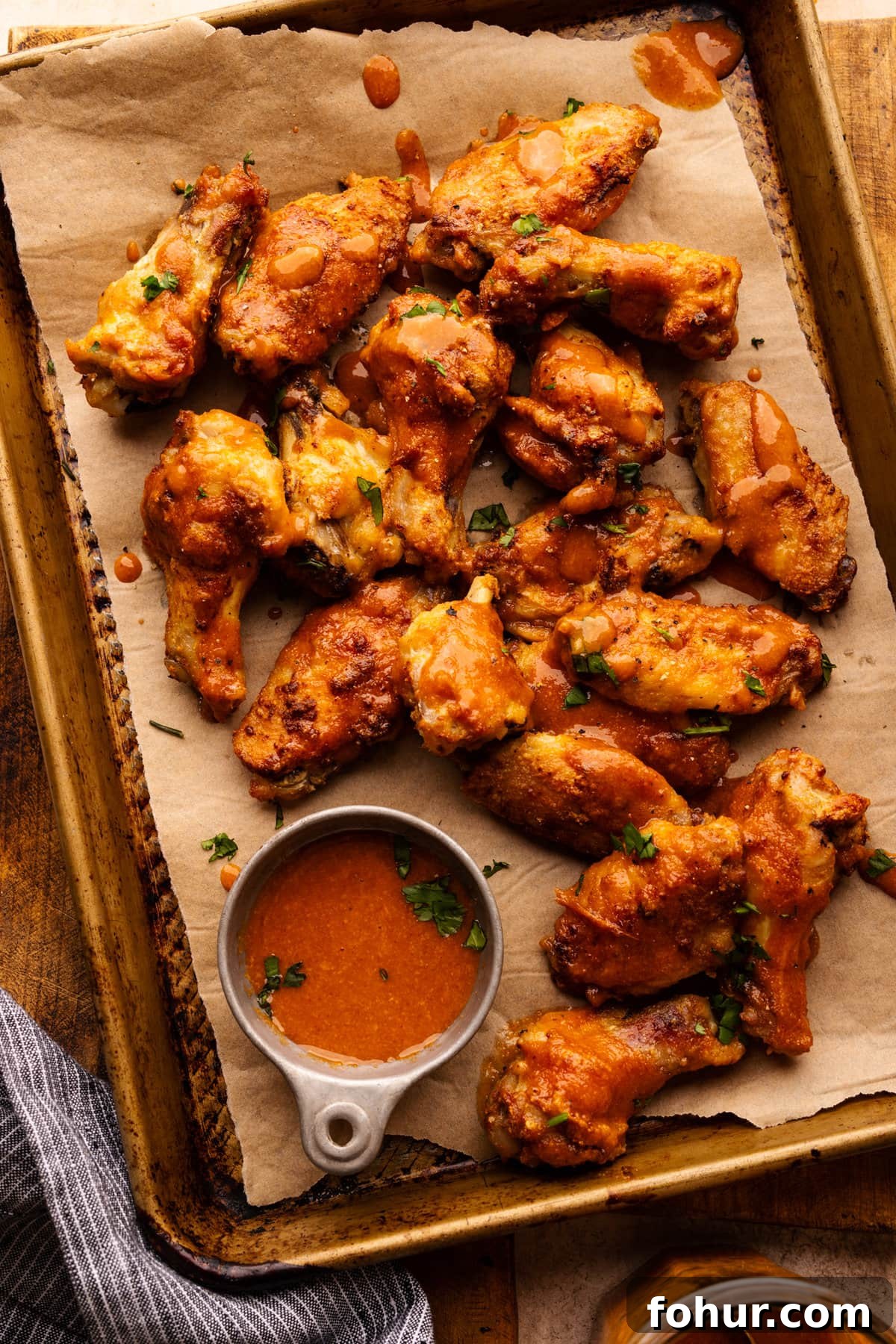 Crispy Oven Baked Chicken Wings Recipe 2 Chicken wings arranged on a pan lined with parchment paper and a small bowl of sauce next to it.