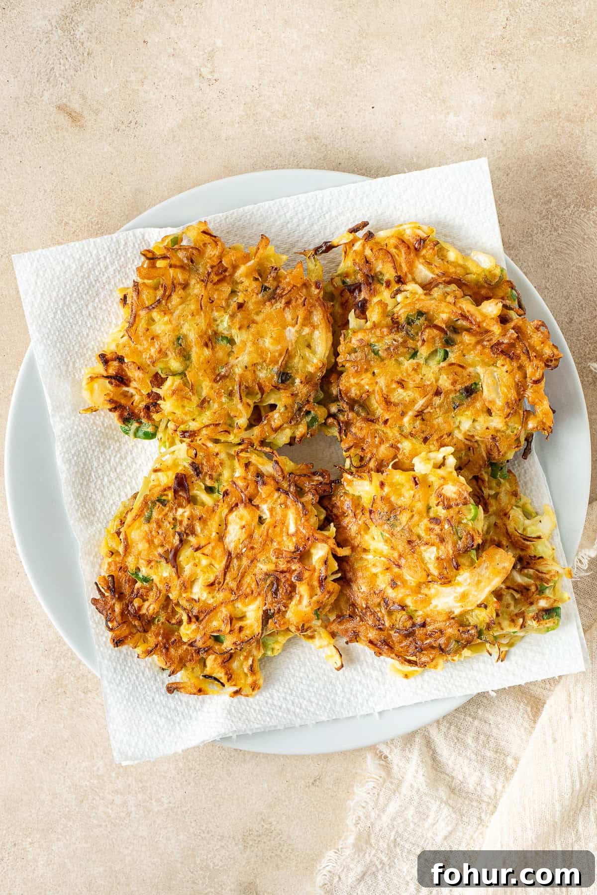 Crispy Cabbage Fritters Recipe with Tangy Yogurt Dip 8 The cooked cabbage fritters on a plate lined with paper towel.