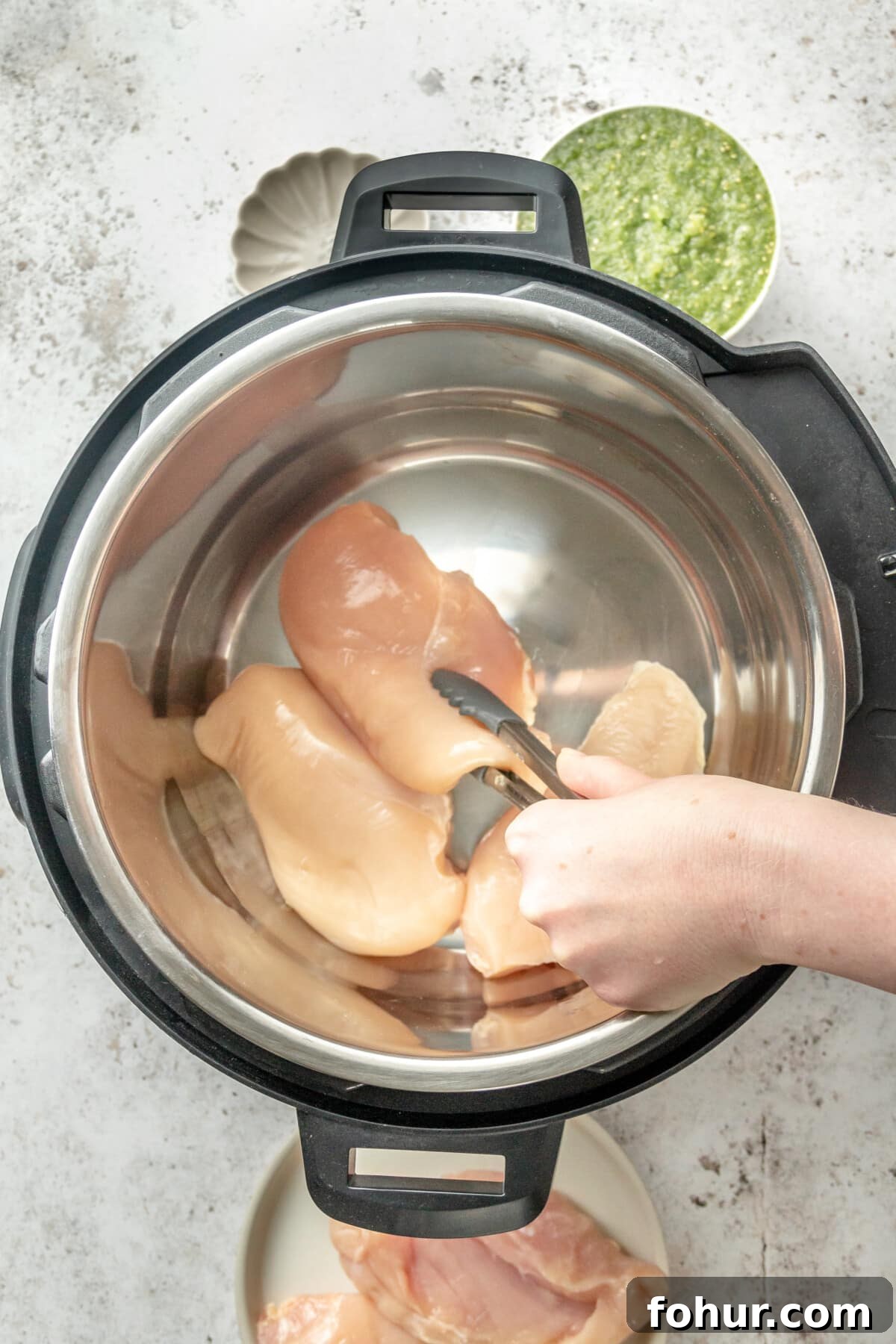 Instant Pot Salsa Chicken Recipe for Tacos and Meal Prep 3 Chicken breasts are placed into an instant pot sitting on a light grey surface.
