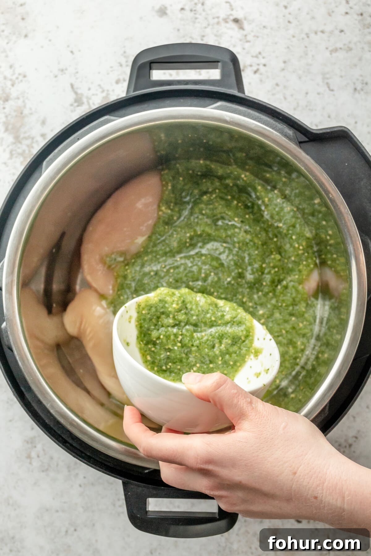 Instant Pot Salsa Chicken Recipe for Tacos and Meal Prep 4 Salsa verde is poured over chicken breasts sitting in an instant pot on a light grey surface.