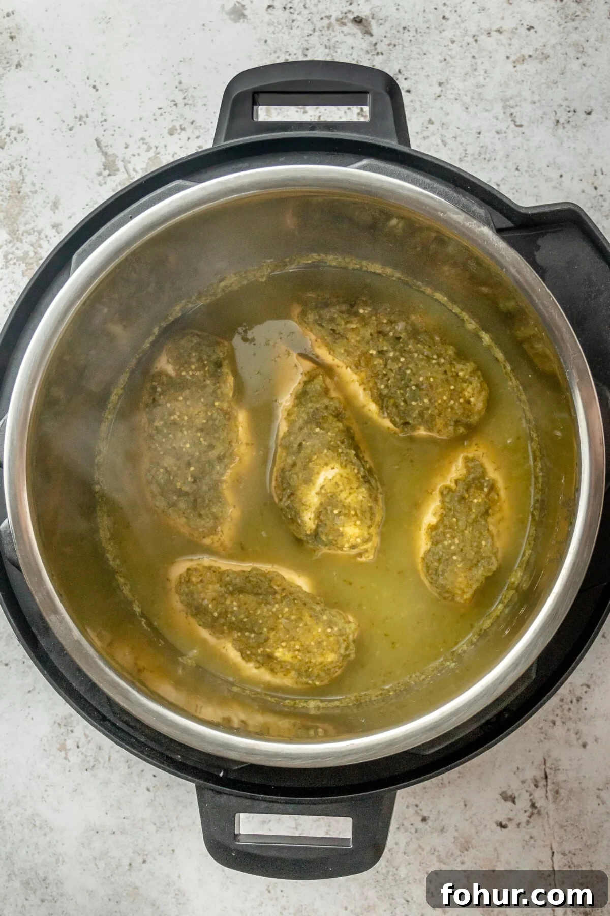 Instant Pot Salsa Chicken Recipe for Tacos and Meal Prep 5 Salsa chicken breasts sit in an instant pot coated in salsa verde on a light grey surface.