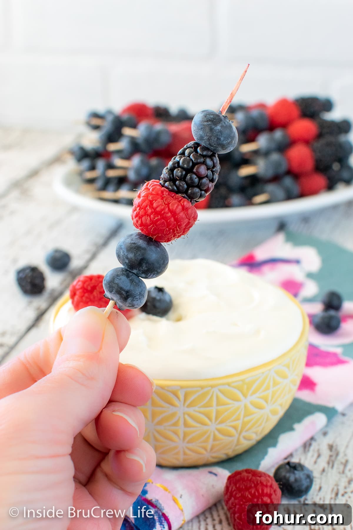 A bowl of fruit dip and fruit skewers.
