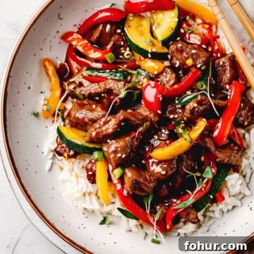 Beef stir fry with Asian sauce, and peppers with rice in a bowl.