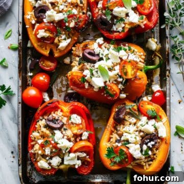 Stuffed peppers with rice and tomatoes topped with feta and herbs on a baking tray.