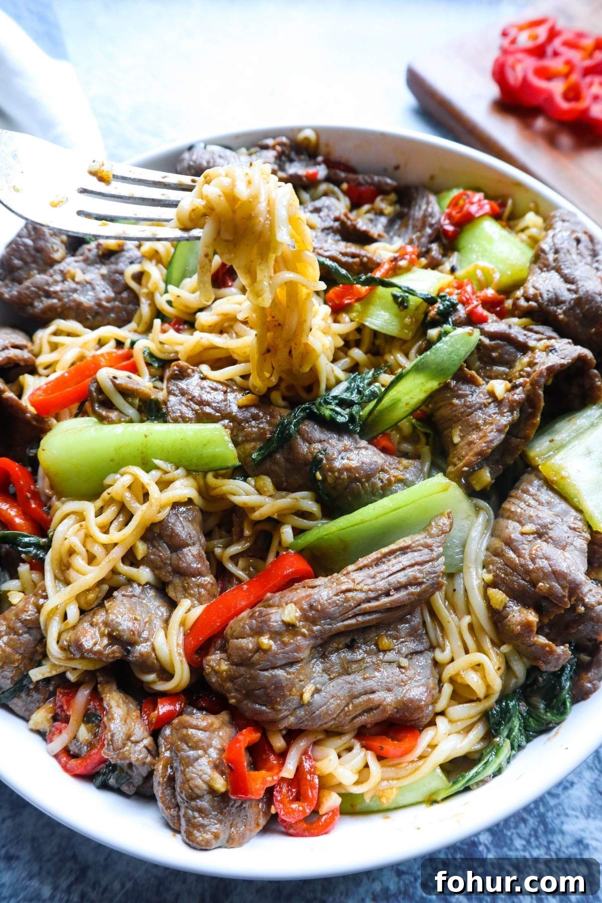 Pho Xao: Vietnamese Stir-Fried Beef and Rice Noodles 7 white plate with fork pulling noodles surrounded by vegetables and beef.